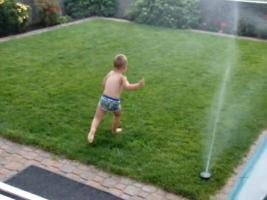 Toddler boy has fun running through sprinklers